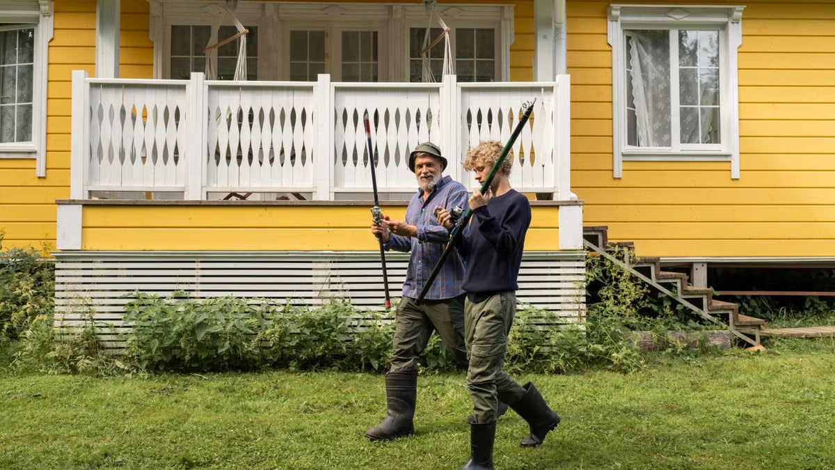 Elderly man and young boy with fishing rods in front of a yellow house, spending quality time outdoors.