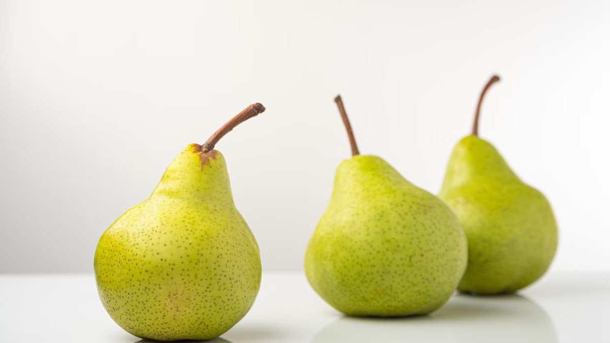Three organic pears on a reflective white surface showcasing freshness and simplicity.